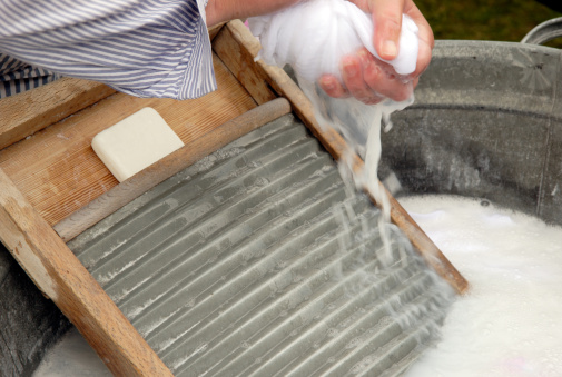 Old style washboard washing in zinc tub with  senior hands squeezing lye out of rag