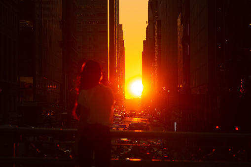 Woman standing at overpass looking at sunset in midtown Manhattan.