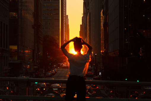 Woman standing at overpass looking at sunset in midtown Manhattan.