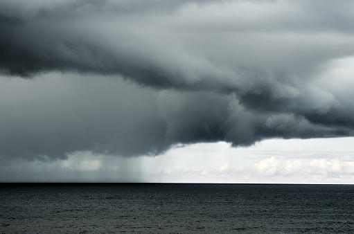 Dramatic cloudy rainy sky over dark water surface sea