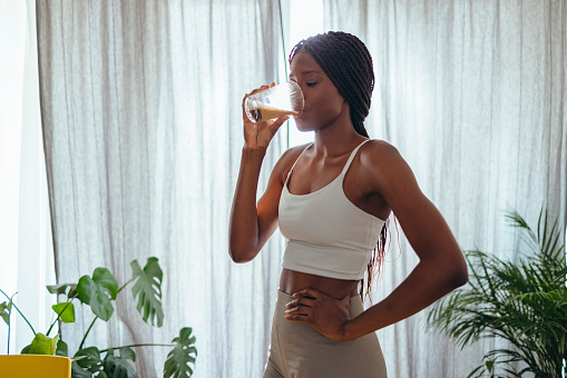 Young African-American woman in sportswear standing in living room and drinking coffee before home workout
