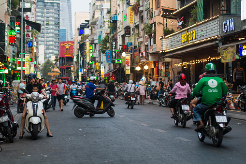 Ho Chi Minh City, Vietnam - 08-06-2019: colorful perspective of Bui Vien Street with numerous hotel, bar and shop sign boards, crowded with people & motorbikes with a view of Bitexco Financial Tower