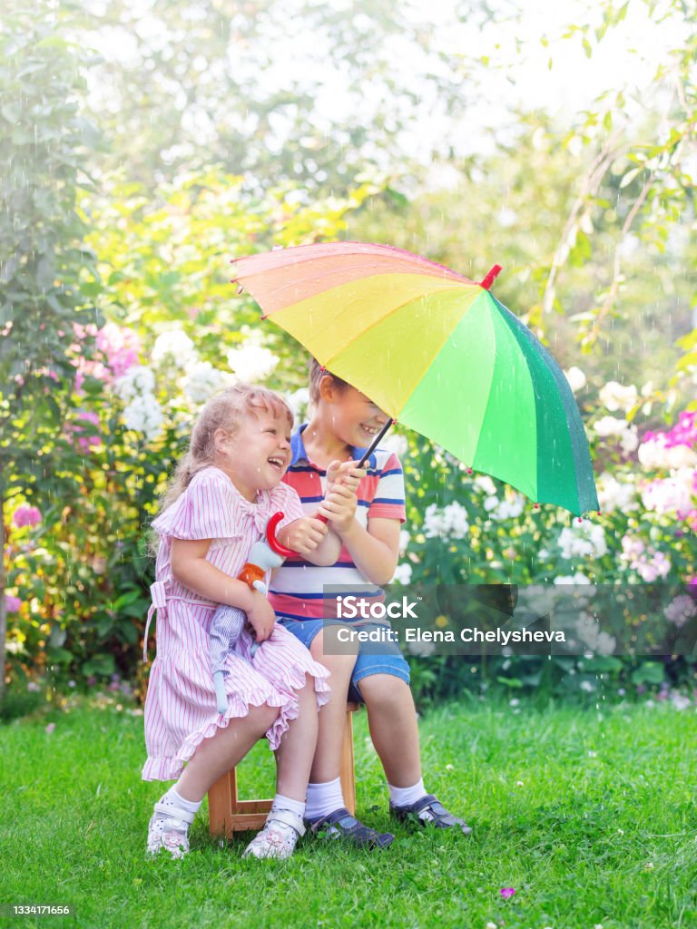 children, brother and sister are standing with an umbrella in the rain Springtime Stock Photo