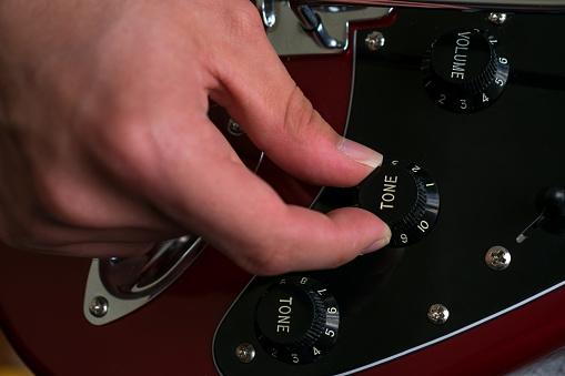 Close-up of an unrecognizable person changing the tone with the tone knob on an electric guitar. Music, unrecognizable person playing.
