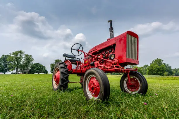 Photo of A vintage red tractor on a green farm field and blue sky with cumulus clouds.