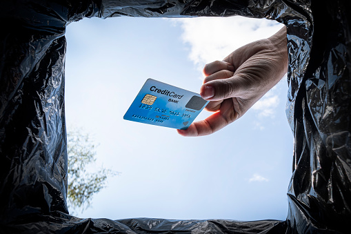 Hand throws credit card into trash bin with package on blue background, bottom view. the concept of abandoning bank transactions and financial loans.