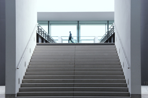 Staircase in modern architecture leading to light window facade with corporate person rushing by