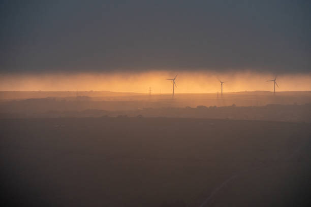 暗い雲の下で夕方の太陽の下で風力タービンのライン - silhouette sunrise non urban scene england ストックフォトと画像