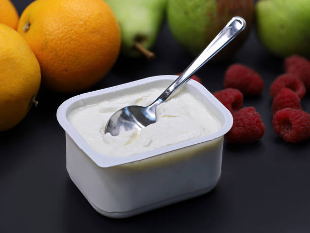 quark or cream cheese in plastic box with spoon on black backround with fruits, healthy nutrition for breakfast quark or cream cheese in plastic box with spoon on black backround with fruits, healthy nutrition for breakfast. curd cheese stock pictures, royalty-free photos & images