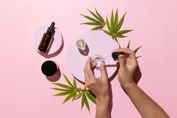 bottles with cbd oil, thc tincture and cannabis leaves on pink background. alternative cosmetics medical concept - druppelfles stockfoto's en -beelden