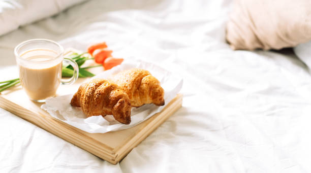 istock Croissant and coffee on white bed on wicker tray with flowers 1334237947