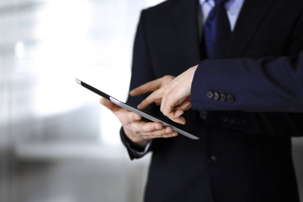 istock Business people use a tablet computer for discussion of their new project, standing in a modern office. Unknown businessman or male entrepreneur with a colleague at workplace. Teamwork and partnership concept 1334248294