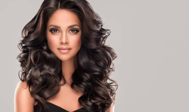 Portrait of perfectly looking young black haired woman with long, curly hairstyle, wearing in exquisite makeup. Perfect looking young woman face wearing in splendid evening makeup is surrounded by dense curls of long black hair. Brunette with elegant wavy hairstyle. Hairdressing art, hair care and makeup. black hair stock pictures, royalty-free photos & images