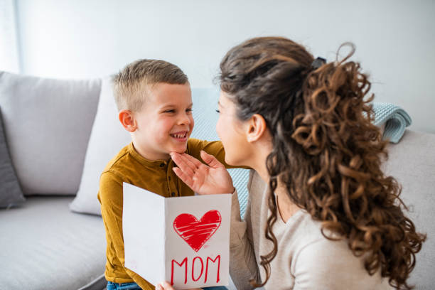 istock Cheerful mother hugging son and reading handmade greeting card with heart while resting on bed during holiday celebration mothers day at home. 1334248538