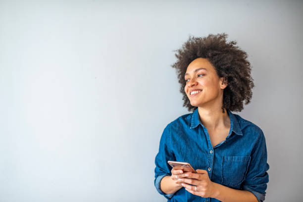 Smiling woman using smartphone isolated on gray wall with copy space.