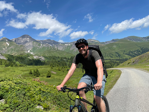 Young man riding an electric mountain bike in the Swiss Alps. He's going downhill.