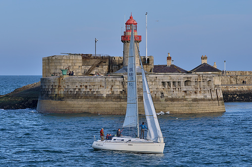 Dublin, Ireland - April 24, 2021: Beautiful creative evening view of sailboat passing in front of red East Pier lighthouse in Dun Laoghaire harbor.  Soft and selective focus