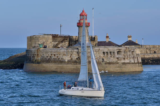 Beautiful creative evening view of sailboat passing in front of red East Pier lighthouse in Dun Laoghaire harbor stock photo