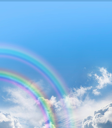 two beautiful rainbow arcs on left, blue sky above and fluffy clouds below creating copy space background for special messages