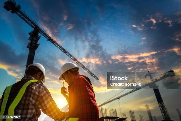 Construction Engineers Discussion With Designer At Construction Site Or Building Site Of Highrise Building With Blueprints Stock Photo - Download Image Now