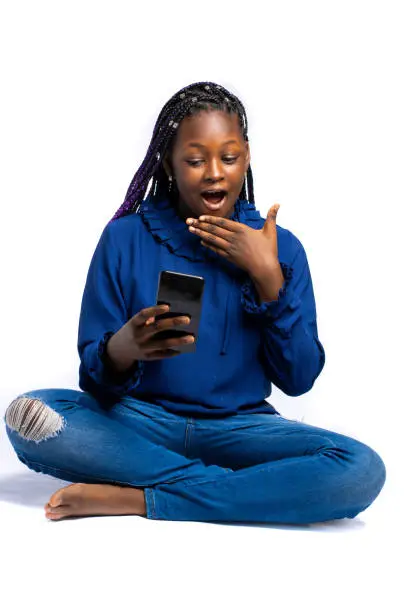 African Teenager looking into her smartphone surprised or shocked while squatting