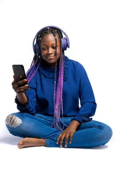 A smiling African Teenager listening to music via wireless headphones connected to a smartphone while squatting