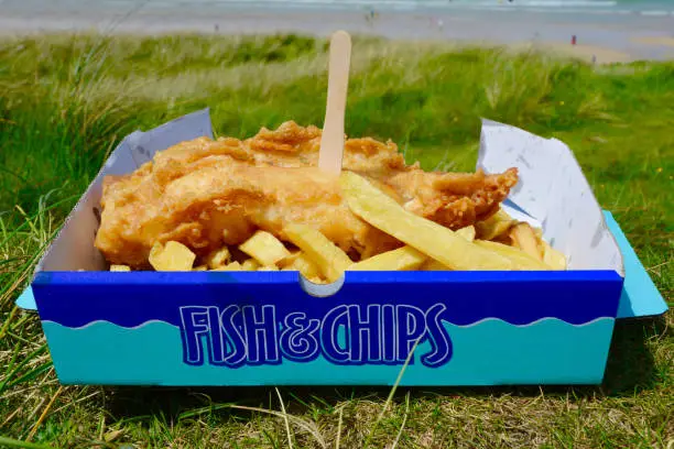 Fish and Chips  close up with a lemon slice with beach in the background