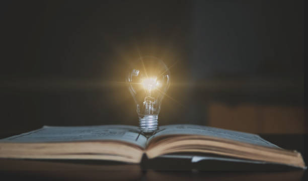 istock Glowing light bulb on a book in concept of idea innovation and inspiration. 1334267183