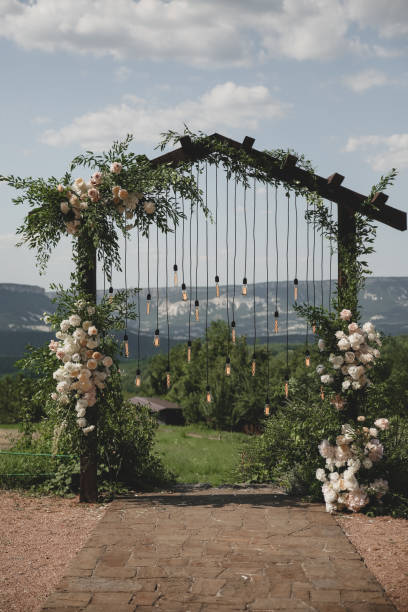 istock Wedding arch on boho style with white flowers in park with light bulbs. 1334267447