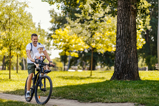 An active family day in nature. A father and son ride a bike through the woods on a sunny summer day. A cute boy is sitting in a bicycle basket while he rides a bicycle. They enjoy the ride