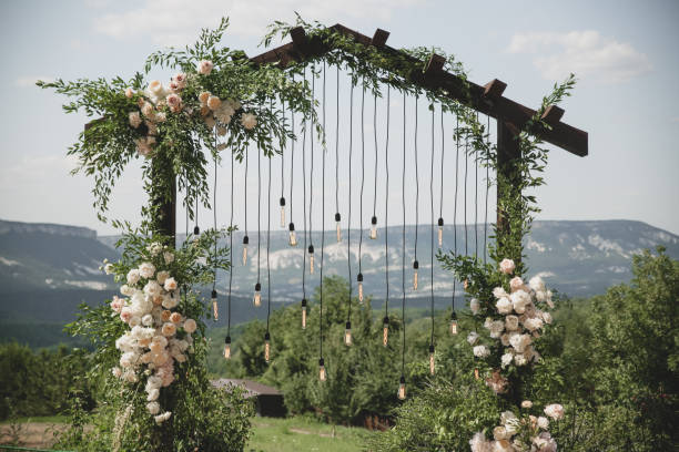 istock Wedding arch on boho style with white flowers in park with light bulbs. 1334267501