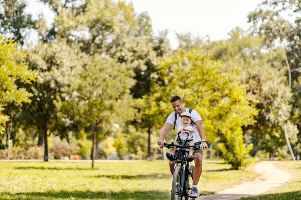 istock Dad and son ride their bikes through the woods. A little boy sits in a bicycle basket while his father leads him through the woods. Summer sunny family day they are both smiling. Happy family moments 1334267512