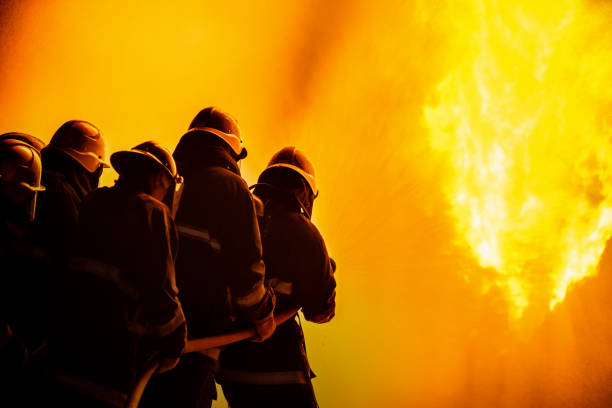 istock Firefighter using extinguisher or Twirl water fog type fire extinguisher to spray water from hose for fire fighting with fire flame on fuel and control fire for safety in plant of industrial area. 1334272646