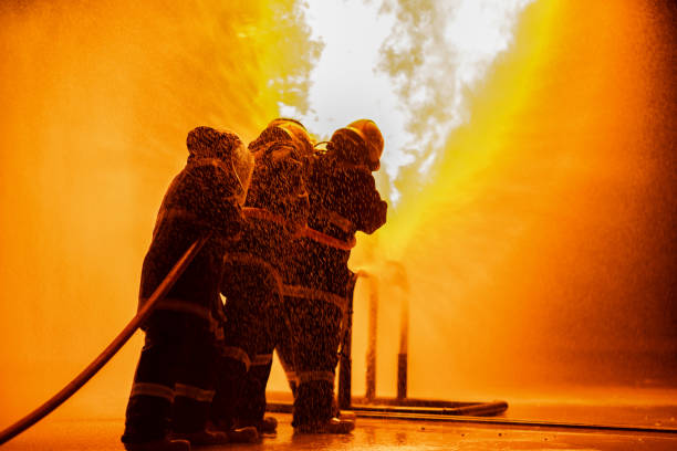 istock Firefighter using extinguisher or Twirl water fog type fire extinguisher to spray water from hose for fire fighting with fire flame on fuel and control fire for safety in plant of industrial area. 1334272651