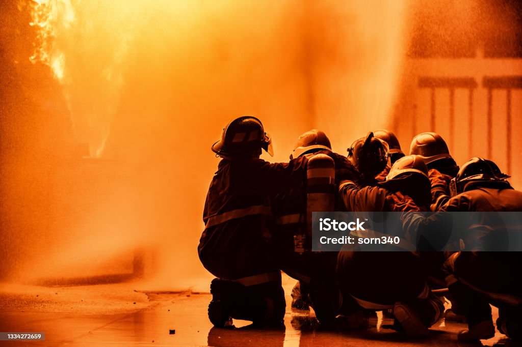 Firefighter using extinguisher or Twirl water fog type fire extinguisher to spray water from hose for fire fighting with fire flame on fuel and control fire for safety in plant of industrial area. Firefighter Stock Photo