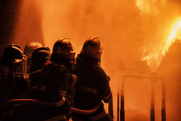 istock Firefighter using extinguisher or Twirl water fog type fire extinguisher to spray water from hose for fire fighting with fire flame on fuel and control fire for safety in plant of industrial area. 1334272662
