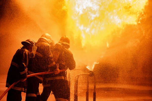 istock Firefighter using extinguisher or Twirl water fog type fire extinguisher to spray water from hose for fire fighting with fire flame on fuel and control fire for safety in plant of industrial area. 1334272682
