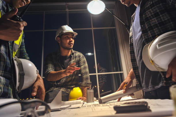 Construction engineers discussion with architects at the meeting room with Blueprint Architecture on       Desk, Working overtime, Compulsory overtime. stock photo