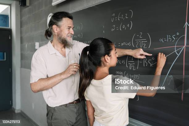 Latin Female Teenager Student Doing Maths Geometry Exercises On Blackboard With Help Of Friendly Professor In High School Stock Photo - Download Image Now