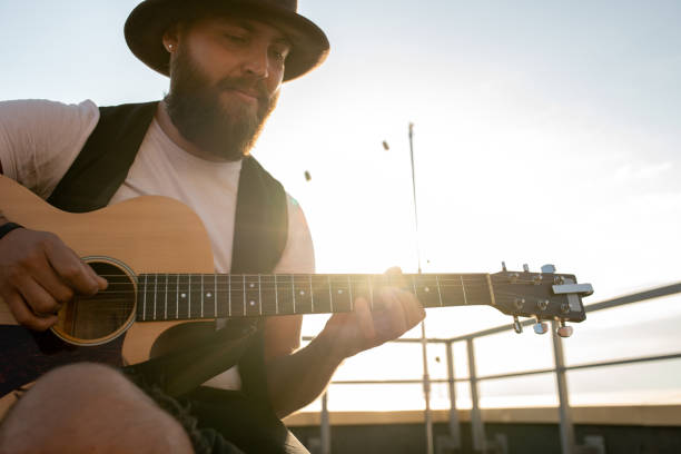 istock Young bearded man playing guitar on rooftop patio 1334277040