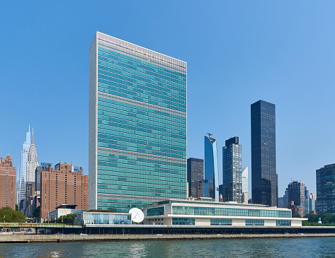 New York, NY - July 27, 2021: The United Nations Headquarters buildings on the east side of Manhattan, NYC. The buildings are seen from the East River. Prominent is the 39 story United Nations Secretariat Building (1952) designed architects Oscar Niemeyer and Le Corbusier.