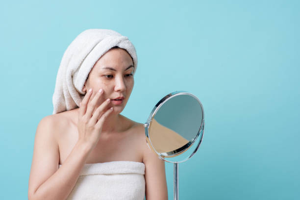 Beautiful Asian young woman touching face and was a feeling of anxiety on her face while looking at the mirror. Skincare and clean concept, Beauty treatment process for rejuvenation. stock photo