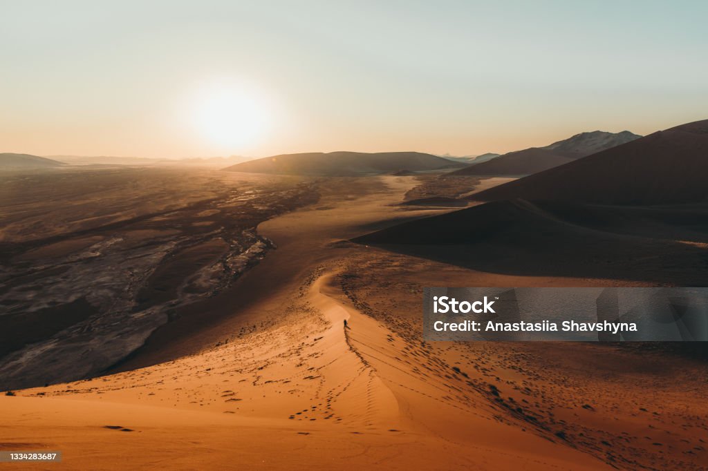 Man traveler enjoyimeetsng the scenic sunset at the sand dunes in Namib desert Silhouette of a man walking on the top of the big dune enjoying the dramatic bright desert sunset at Anmib-Naukluft National park Desert Area Stock Photo