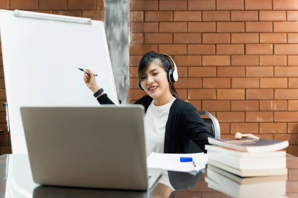 istock Asian tutor teacher sitting at table online teaching or explaining lesson to students her group with whiteboard in class room. Modern education remotely, Quarantine training, Online training concept. 1334283943