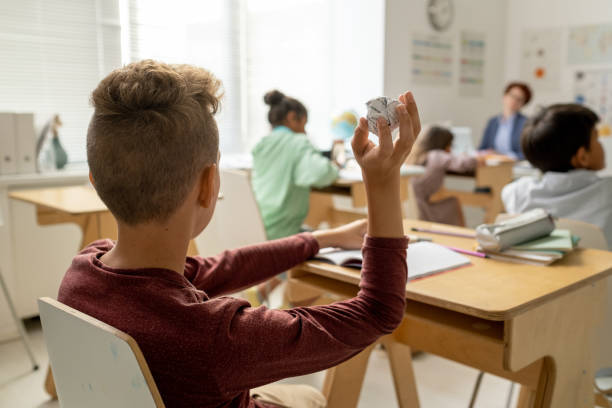 istock SChoolboy holding crampled paper in hand while sitting by desk 1334284297