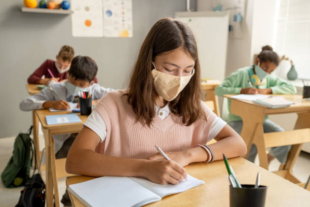istock Cute schoolgirl in protective mask making notes 1334284346
