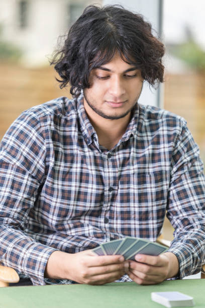 21-year-old South Asian man wearing a checked shirt playing cards.