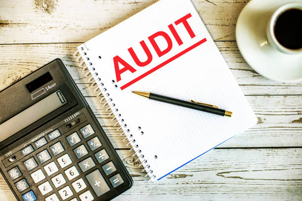 istock The audit is written in red on a white notebook that lies on a light wooden table between a calculator and a cup of coffee 1334296733