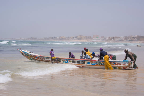 Dakar, Senegal - June 01, 2014: Group of fishermen pushing a fishing boat from the sand to the sea on the beaches of Yoff