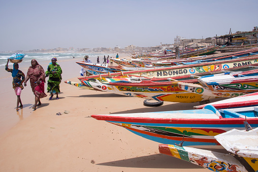 Dakar, Senegal - June 01, 2014: Polychrome fishing boats washed up on the sand and women hauling fish on the beaches of Yoff